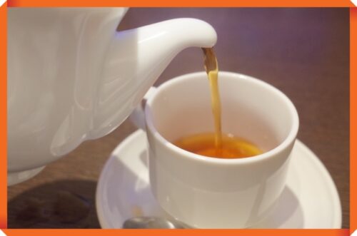 白いポットから白いカップに紅茶が注がれている画像